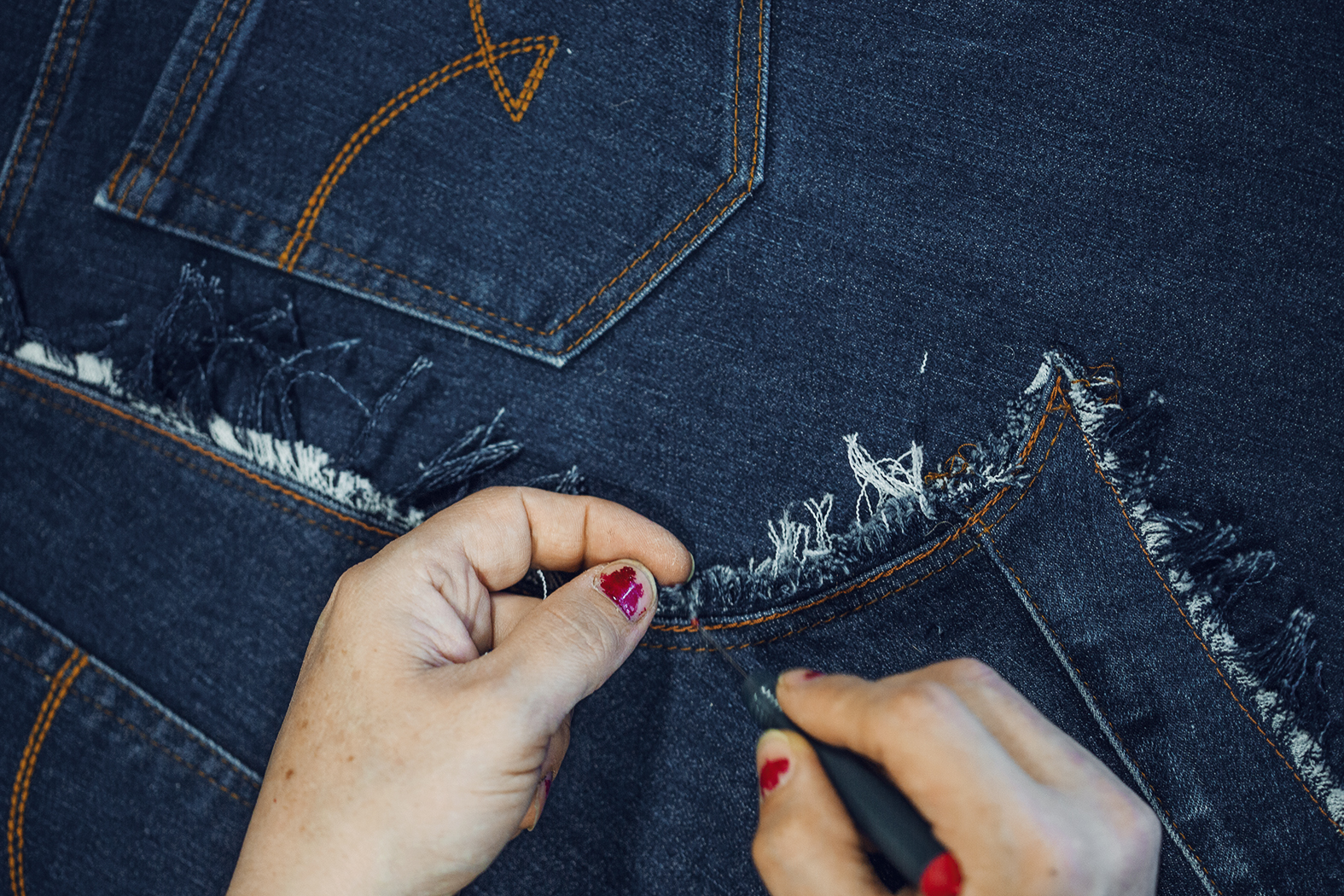 En person syr i jeanstyg
